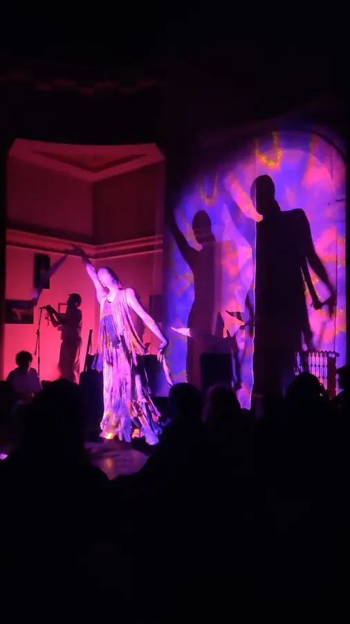 A figure dances while a visual is projected onto them and the background.
