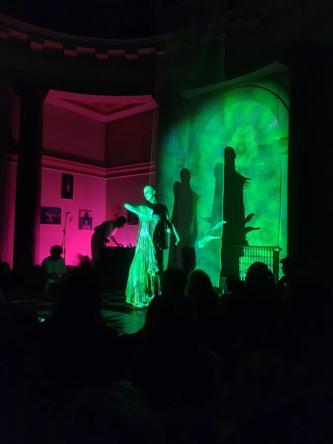 A figure dances while a visual is projected onto them and the background.